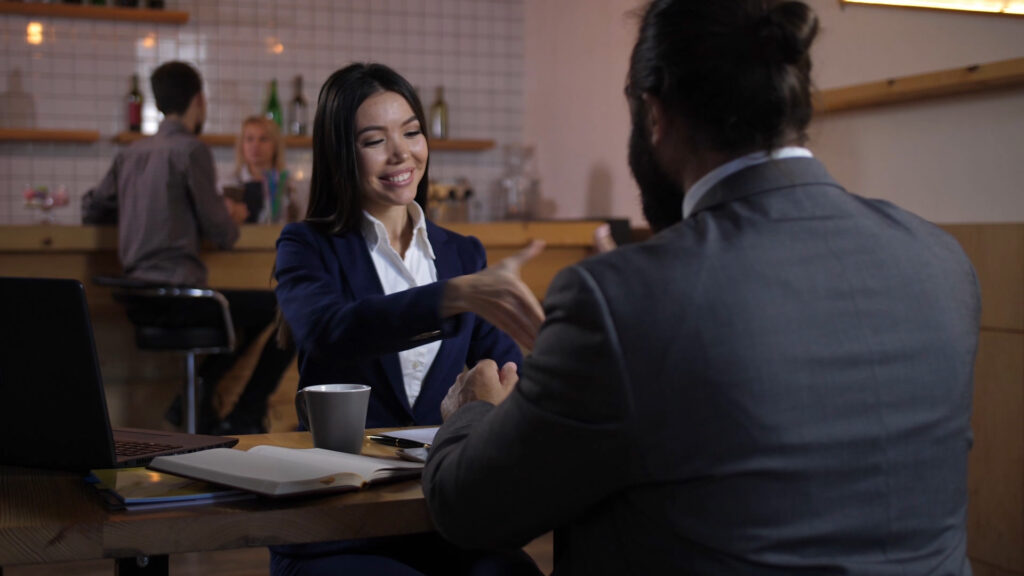 smiling woman and man in business attire, meeting over coffee, about to shake hands