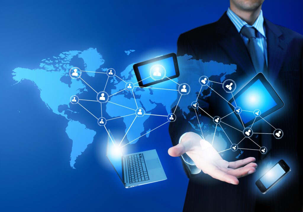 concept photo of various electronic devices floating in mid air, a laptop, 2 tablets, and iPhone, seemingly being levitated by a man's hand, who is in a full, against a blue backdrop with the world map on it