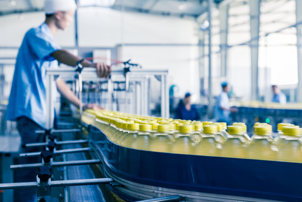 skilled trades worker working in a manufacturing environment, with a conveyor belt going by with what appears to be bottled beverages with yellow lids