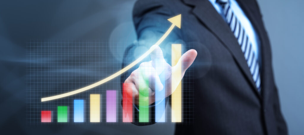 concept design of a graph bar graph exhibiting growth and a yellow arrow indicating an upward trend, overlaid against a person in a suit pointing at said arrow, on a dark blue background