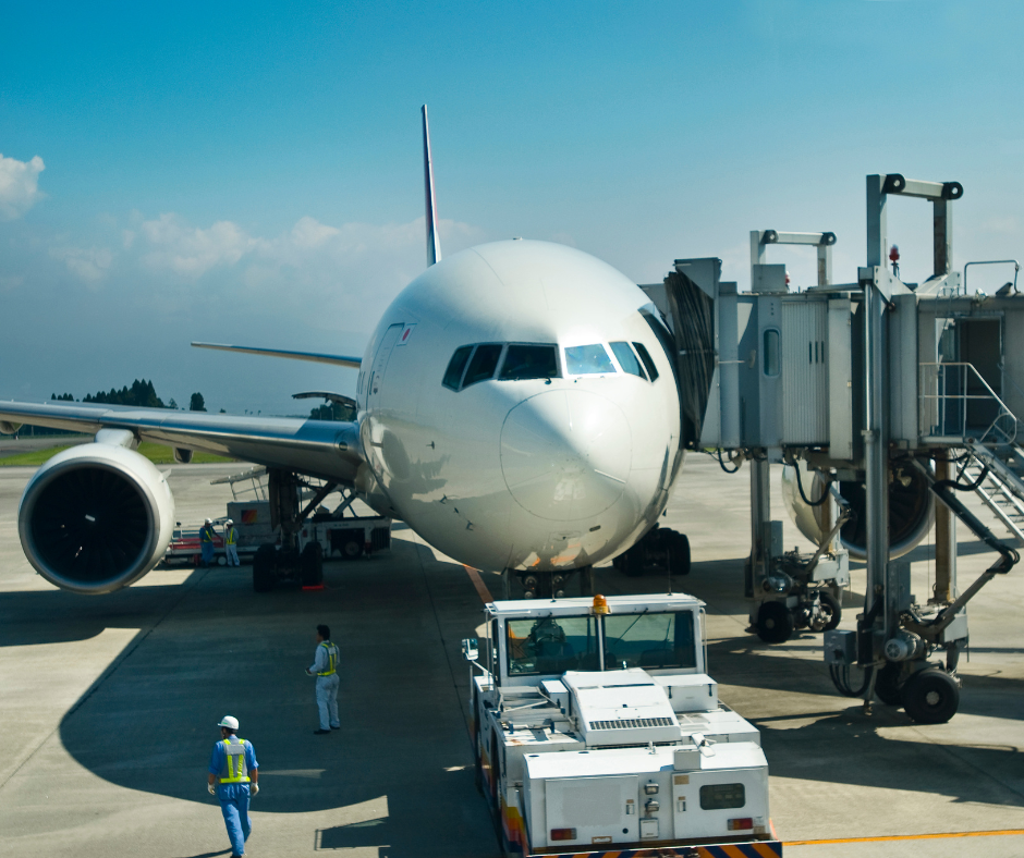 airplane docked at airport on the tarmac, airline employees stand beneath plane