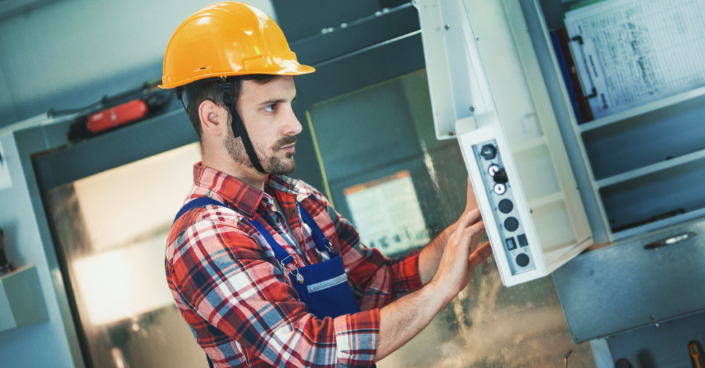 man in yellow hardhat attending to a machine via a control panel
