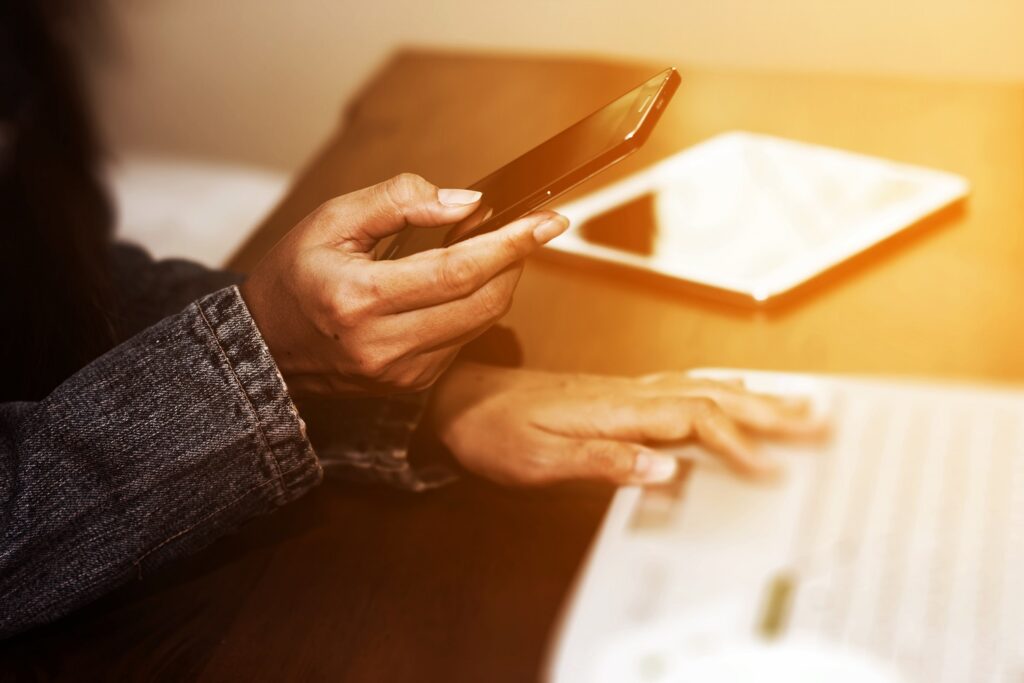 sephia filter of person's hands, one holding a cell phone as if checking it for a notification, the other hand on a piece of paper