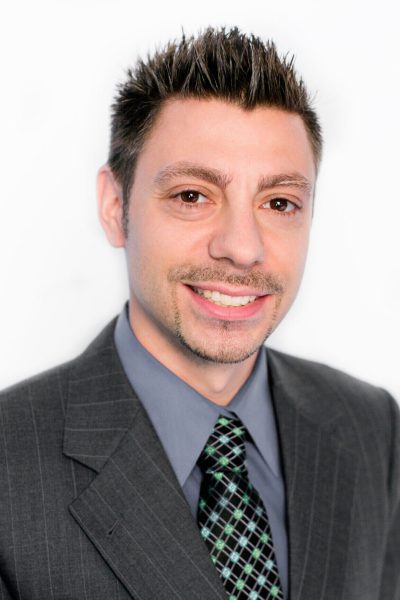 Photo of Andrew Stapinski, charcoal blue suit, light grey dress shirt, dark blue tie with green dots, smiling